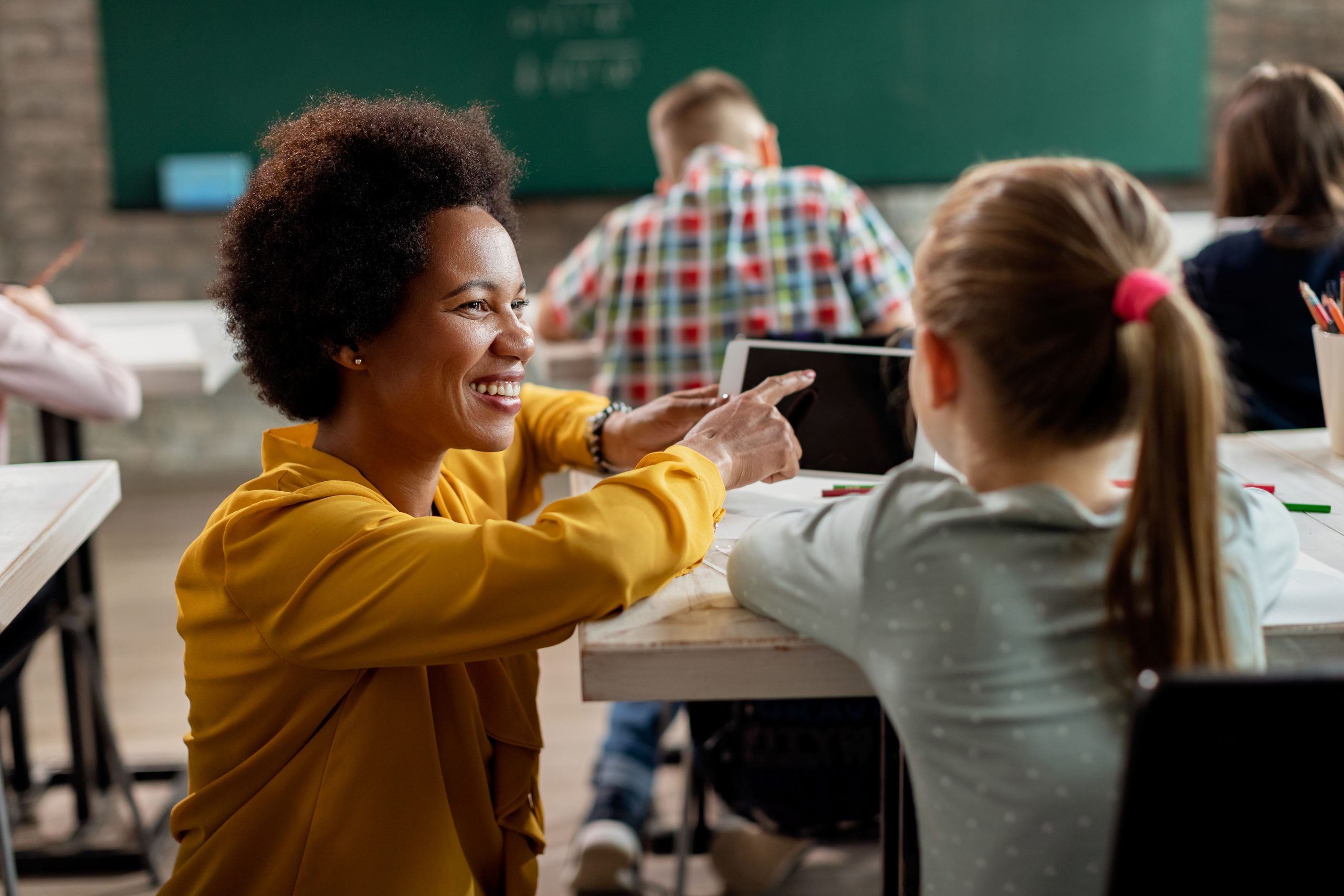 Happy black teacher and schoolgirl using digital tablet in the c